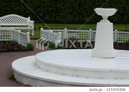 White garden sundial and bench in peaceful park setting White garden sundial and bench in peaceful park setting 125845866
