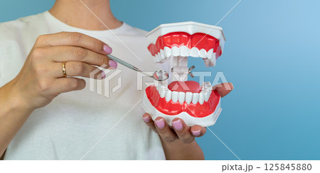 Female holding dental model with mirror for oral health education on blue background Female holding dental model with mirror for oral health education on blue background 125845880