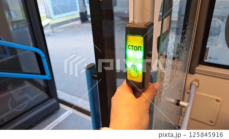 Moscow, Russia - April 26, 2025.Hand pressing stop button with cyrillic text on public bus exit 125845916