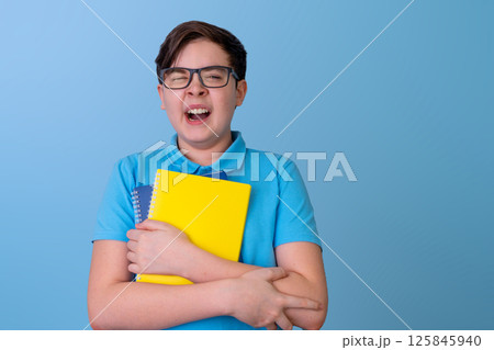 Caucasian Teen Boy with glasses with colorful laptops in a blue shirt, yawns with fatigue 125845940