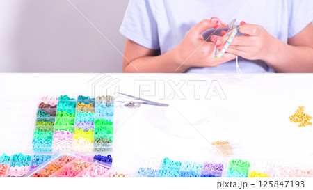 Delicate fingers of a young girl navigate through a treasure trove of bright, multicolored beads, each compartment revealing a new hue to choose from. 125847193