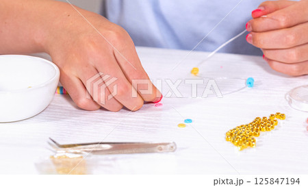 Delicate fingers of a young girl navigate through a treasure trove of bright, multicolored beads, each compartment revealing a new hue to choose from. She's immersed in the joyful task of stringing 125847194