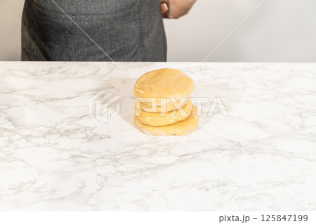 Front view of Classic Sugar Cookie Dough on a marble countertop, freshly mixed and ready for wrapping before chilling. The dough is lightly shaped, with the mixing bowl and spatula partially visible 125847199