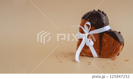 Present gift tied bow holiday Valentine's Day birthday celebration Heart shaped dark chocolate croissant on beige background with copy space. Puff pastry new trendy sweet dessert bakery. Creamy dough 125847252