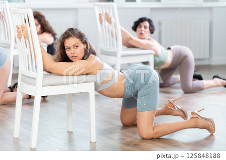 Young woman kneeling on floor during sensual lap dance with chair in group studio Young woman kneeling on floor during sensual lap dance with chair in group studio 125848188