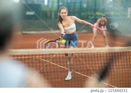 Sporty young girl playing doubles tennis on outdoor court 125848231