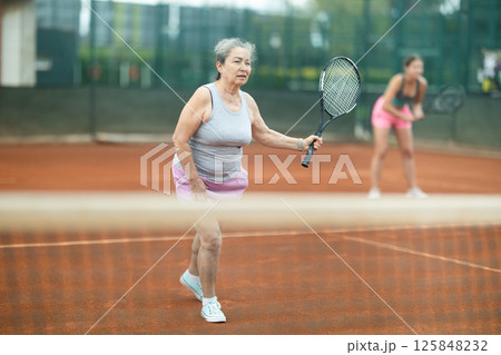 Young and elderly women playing doubles tennis 125848232