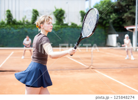 Young woman playing doubles tennis on court 125848274