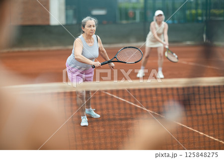 Two elderly women playing doubles tennis Two elderly women playing doubles tennis 125848275