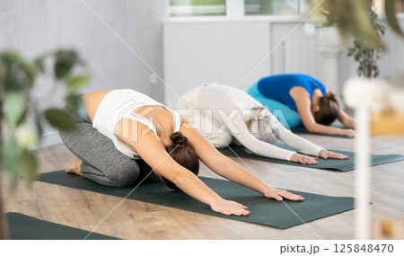 Women of different ages resting in kneeling asana Balasana child pose during group yoga class in studio Women of different ages resting in kneeling asana Balasana child pose during group yoga class in studio 125848470