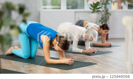 Sportive women of different ages performing various stretching exercises during yoga workout in studio 125848508