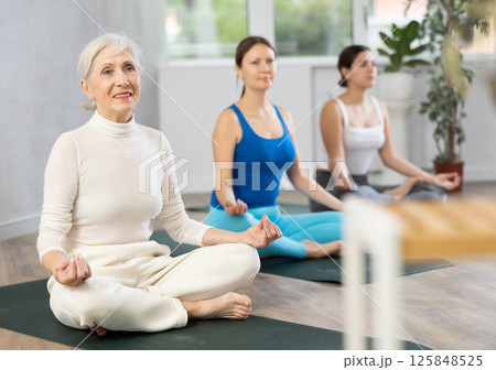 Diligent women practicing lotus pose of yoga in light fitness room 125848525