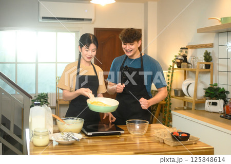 Happy couple preparing to cook pancakes together in a cozy kitchen Happy couple preparing to cook pancakes together in a cozy kitchen 125848614