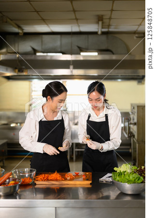 Cooking instructor giving hands on guidance to a student on food preparation. 125848705