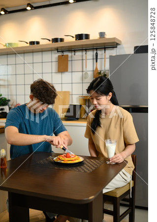 Young couple enjoying a homemade breakfast together with pancakes and a glass of milk Young couple enjoying a homemade breakfast together with pancakes and a glass of milk 125848728