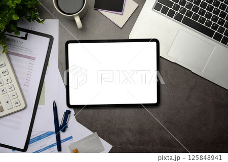 Top view of digital tablet with blank, financial reports, and laptop on stone desk 125848941