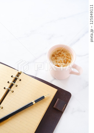 ミルクをたっぷり入れたコーヒー、カフェ・ラッテを飲みながら、システム手帳でデスクワーク中のイメージ 125849111