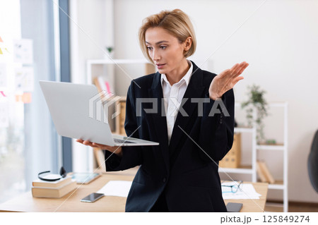 Businesswoman wearing formal attire engaged in work with laptop indoors in modern office space 125849274