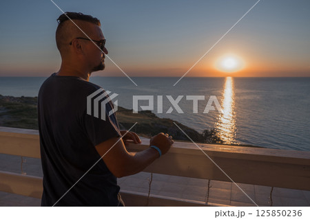 A man in sunglasses swims in a blue pool. Vacation at the hotel by the sea, sunset and mountains. Happy dad, family happiness. Muscles and a beautiful figure, black hair. High quality photo 125850236