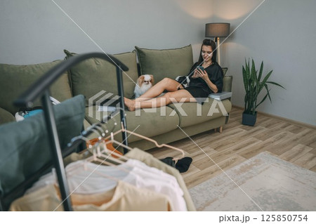 woman relaxing with smartphone during morning beauty routine with japanese chin dogs at home, clothes rack 125850754