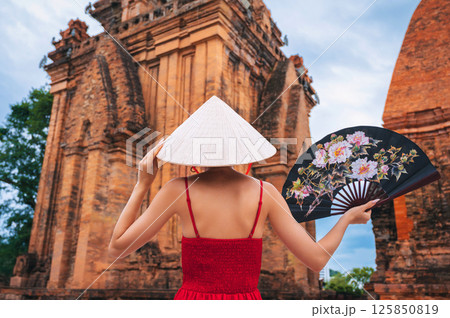 back of an Asian girl tourist traveler in Vietnamese cone hat with a fan on Cham Towers of Po Nagar in Nha Trang in Vietnam in Asia back of an Asian girl tourist traveler in Vietnamese cone hat with a fan on Cham Towers of Po Nagar in Nha Trang in Vietnam in Asia 125850819