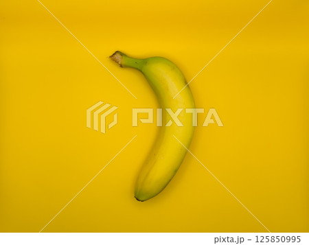 Fresh bright yellow banana on yellow background in the center of the image, top view 125850995