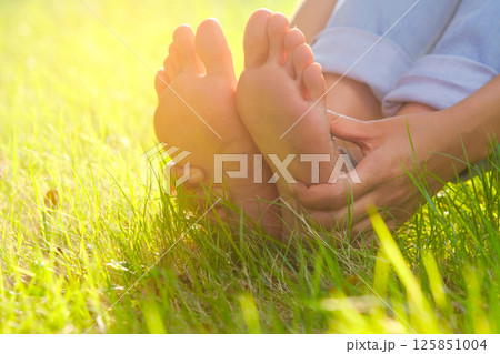 Foot pain .Woman sitting on grass Her hand caught at the foot. Having painful feet and stretching muscles fatigue To relieve pain. health concepts. 125851004
