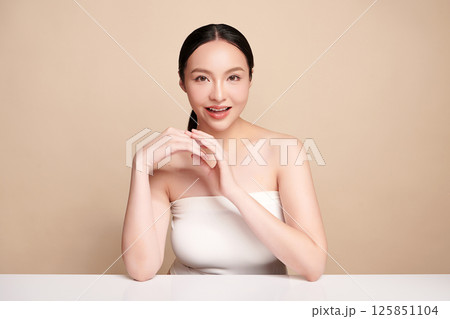 A beautiful young Asian woman with clean, fresh skin against a beige background. Skincare, facial treatment, cosmetology, beauty, and spa. An elegant portrait of an Asian woman. 125851104
