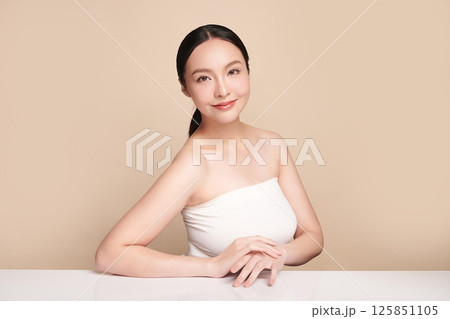 A beautiful young Asian woman with clean, fresh skin against a beige background. Skincare, facial treatment, cosmetology, beauty, and spa. An elegant portrait of an Asian woman. 125851105