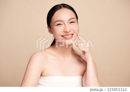 A beautiful young Asian woman with clean, fresh skin against a beige background. Skincare, facial treatment, cosmetology, beauty, and spa. An elegant portrait of an Asian woman. 125851112