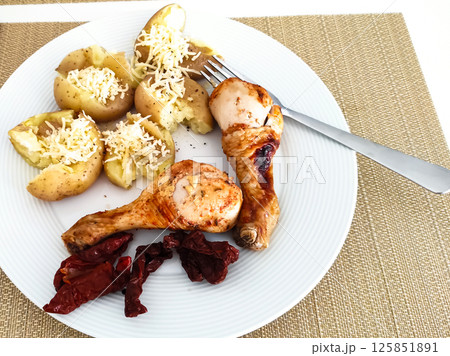 Deliciously arranged plate featuring baked potatoes, grilled chicken, and sun-dried tomatoes for a satisfying meal experience 125851891