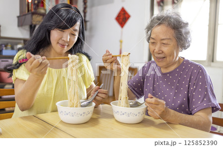 Happy senior mother and daughter eating noodles at home Happy senior mother and daughter eating noodles at home 125852390