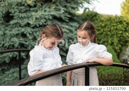 The girls stand very close, leaning toward the tiny snail. The harmony in their outfits and hairstyles highlights their kinship The girls stand very close, leaning toward the tiny snail. The harmony in their outfits and hairstyles highlights their kinship 125852700