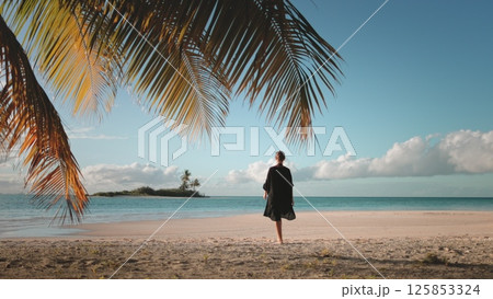 Young woman is enjoying a peaceful moment on a tropical beach, with palm trees swaying gently in the background and the sun setting over the ocean 125853324