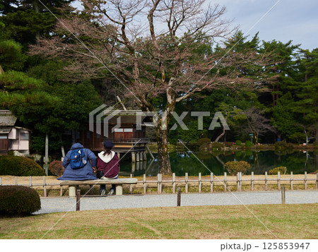 冬の兼六園の霞ヶ池の近くで休憩する男女観光客の姿 125853947