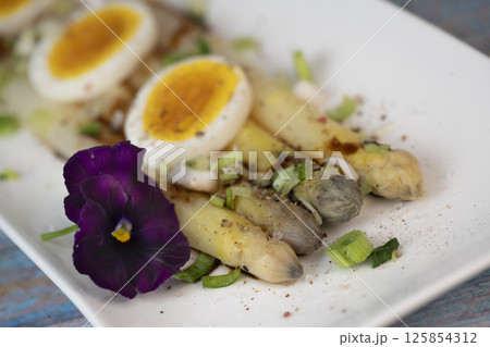 Baked asparagus with boiled egg in big white plate on blue background 125854312