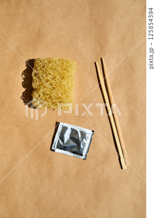 Dry instant noodles with wooden chopsticks and seasoning packet over brown background. Dry instant noodles with wooden chopsticks and seasoning packet over brown background. 125854394