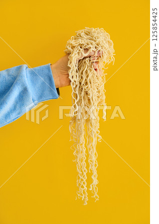 Hand holding clump of long cooked ramen noodles 125854425