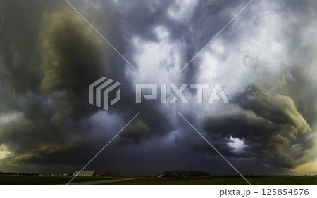 Storm clouds with rain and hail over a road, farm and fields that leads into the distance, creating a very dramatic landscape. Lithuania 125854876