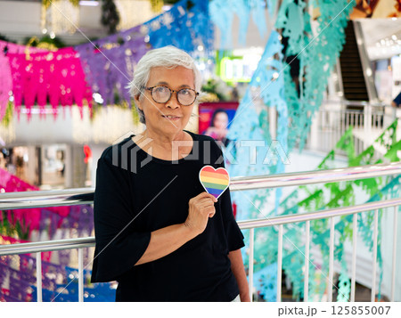 Happy senior Asian woman happy showing rainbow LGBTQ pride heart shape sticker. 125855007