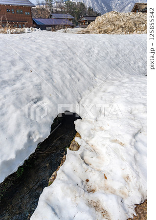 雪解けの白川郷 残雪の中のせせらぎ 125855342