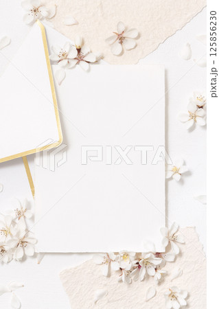 Blank card and envelope near white cherry flowers top view, spring wedding mockup 125856230