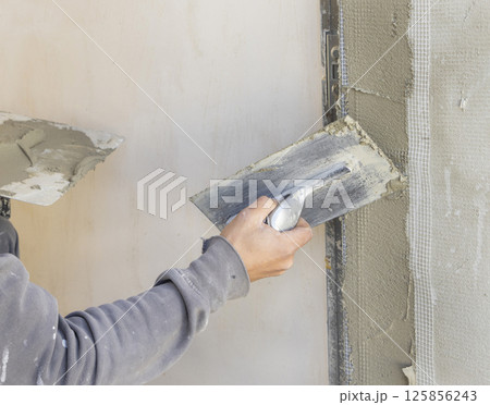 Craftsman uses a float trowel and cement to plaster a house wall. Construction process Craftsman uses a float trowel and cement to plaster a house wall. Construction process 125856243
