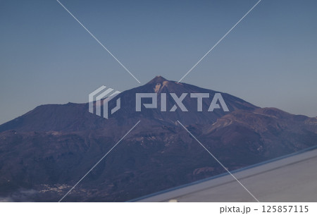Window view from an airplane on the volcano mountain peak of Pico del Teide on Tenerife, Canary Islands, Spain, Europe, EU. High peak of Volcano on blue sky background, copy space Window view from an airplane on the volcano mountain peak of Pico del Teide on Tenerife, Canary Islands, Spain, Europe, EU. High peak of Volcano on blue sky background, copy space 125857115