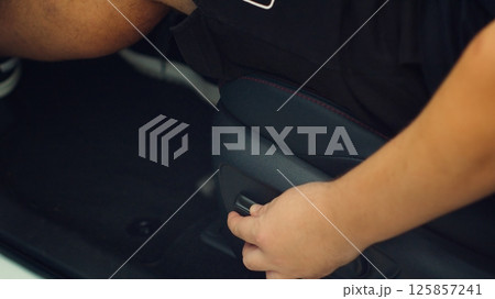 Close up of man in car adjusting driver seat using buttons. Person in vehicle chair that can be raised, lowered, tilted, moved forwards and backwards to suit the comfort of driver Close up of man in car adjusting driver seat using buttons. Person in vehicle chair that can be raised, lowered, tilted, moved forwards and backwards to suit the comfort of driver 125857241