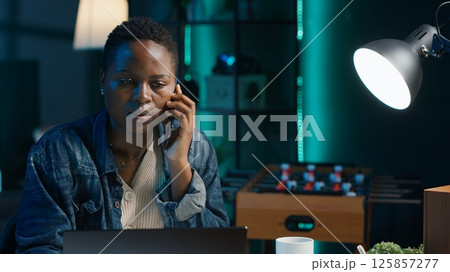 Woman receiving phone call from friend while working from home on laptop in personal office. Freelancer speaking with mate online using cellphone while solving tasks, camera A Woman receiving phone call from friend while working from home on laptop in personal office. Freelancer speaking with mate online using cellphone while solving tasks, camera A 125857277