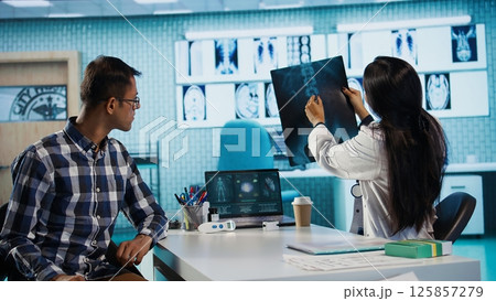 Indian medical staff and male patient engaging in a check up exam with diagnostic tools and test results for scan interpretation. Showcasing healthcare practices and research. Camera B. 125857279