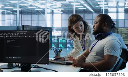 Manager showing admin how to finish tasks in data center providing resources for different workloads. Team leader teaching IT specialist how to while monitor AI supercomputers, camera A 125857298