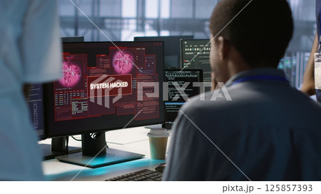 Engineers seeing system hacked popup on PC screen in data center, requesting help from cybersecurity team. Server farm worker seeing security incidents affecting network system, camera A Engineers seeing system hacked popup on PC screen in data center, requesting help from cybersecurity team. Server farm worker seeing security incidents affecting network system, camera A 125857393