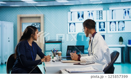 Indian general practitioner and patient engage in a medical consultation with diagnostic tools and x ray text results for scan interpretation. Showcasing healthcare practices and research. Camera B. 125857399
